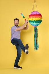 Photo of Emotional man hitting colorful pinata with stick on yellow background