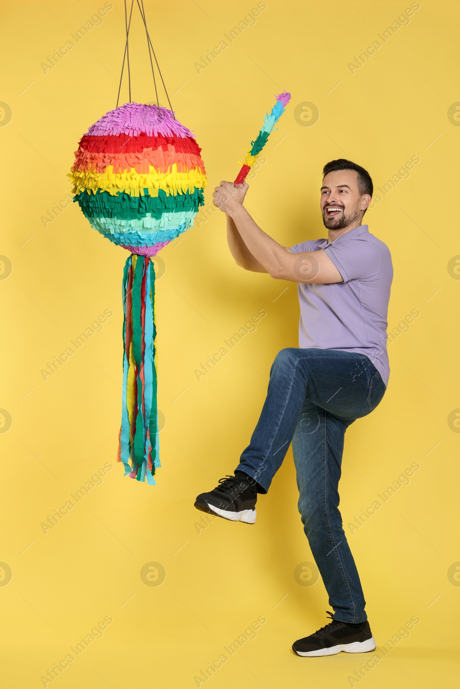 Photo of Emotional man hitting colorful pinata with stick on yellow background