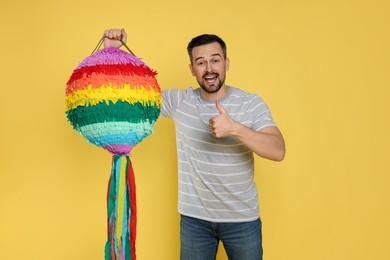 Emotional man with colorful pinata showing thumbs up on yellow background