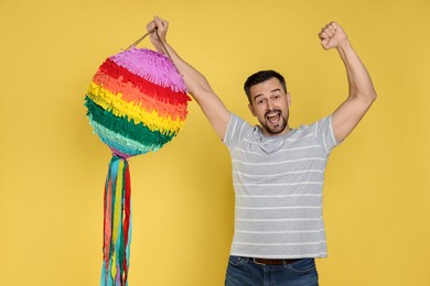 Photo of Emotional man with colorful pinata on yellow background