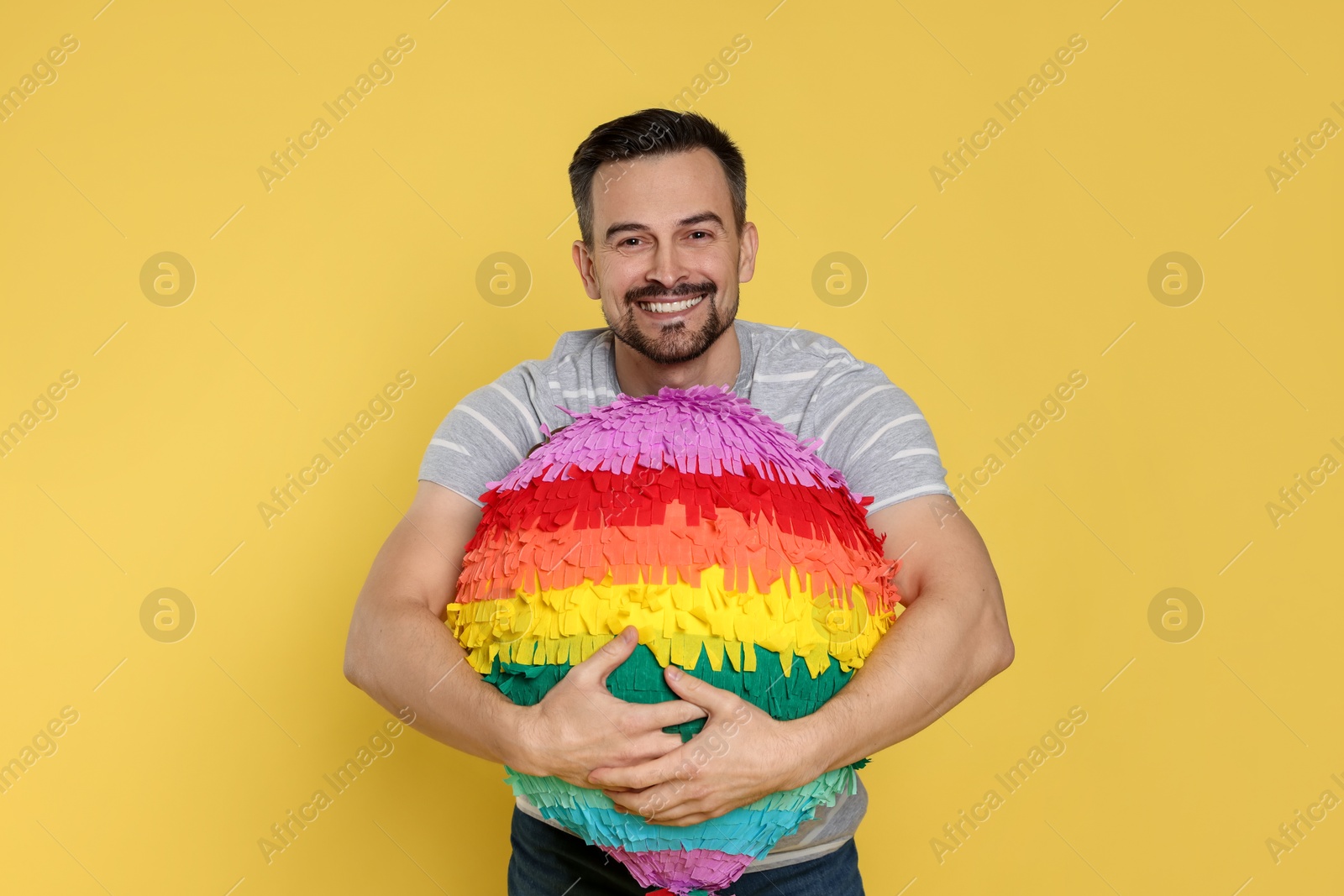 Photo of Happy man with colorful pinata on yellow background