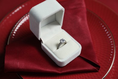 Photo of Beautiful engagement ring and setting for romantic dinner on red background, closeup