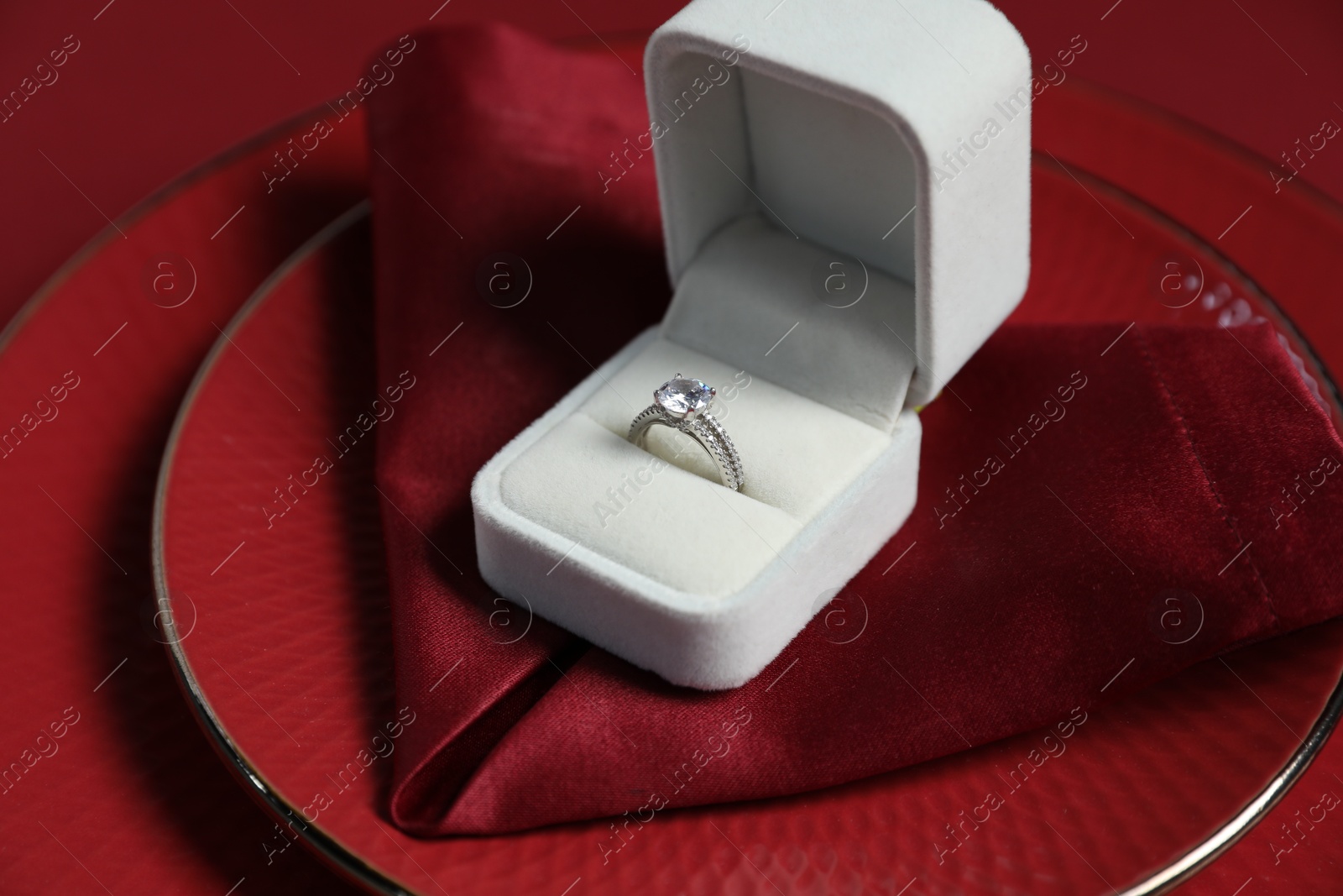 Photo of Beautiful engagement ring and setting for romantic dinner on red background, closeup