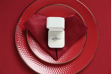 Photo of Beautiful engagement ring and setting for romantic dinner on red background, top view