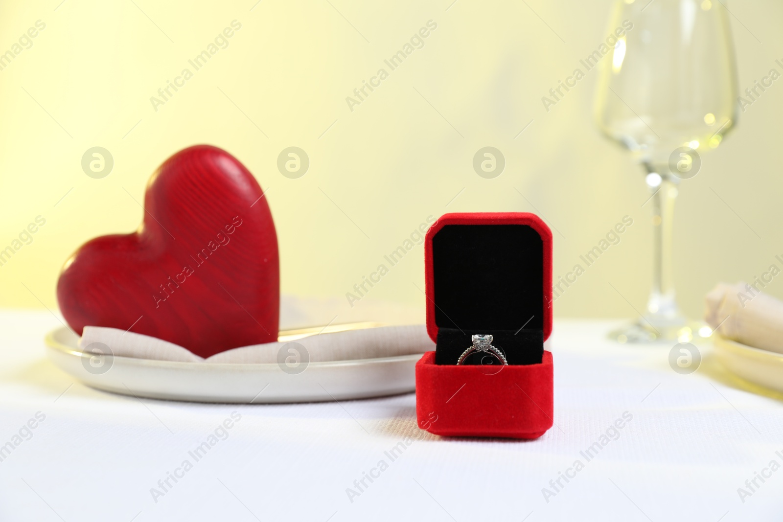 Photo of Beautiful engagement ring and setting for romantic dinner on white table, closeup