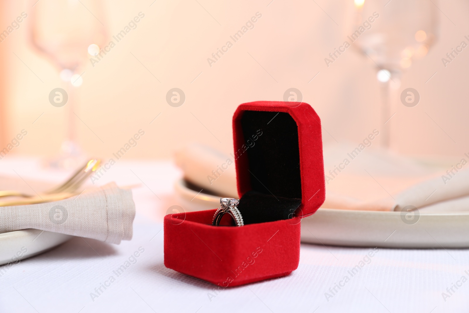 Photo of Beautiful engagement ring and setting for romantic dinner on white table, closeup