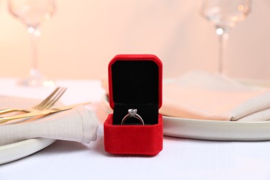 Photo of Beautiful engagement ring and setting for romantic dinner on white table, closeup