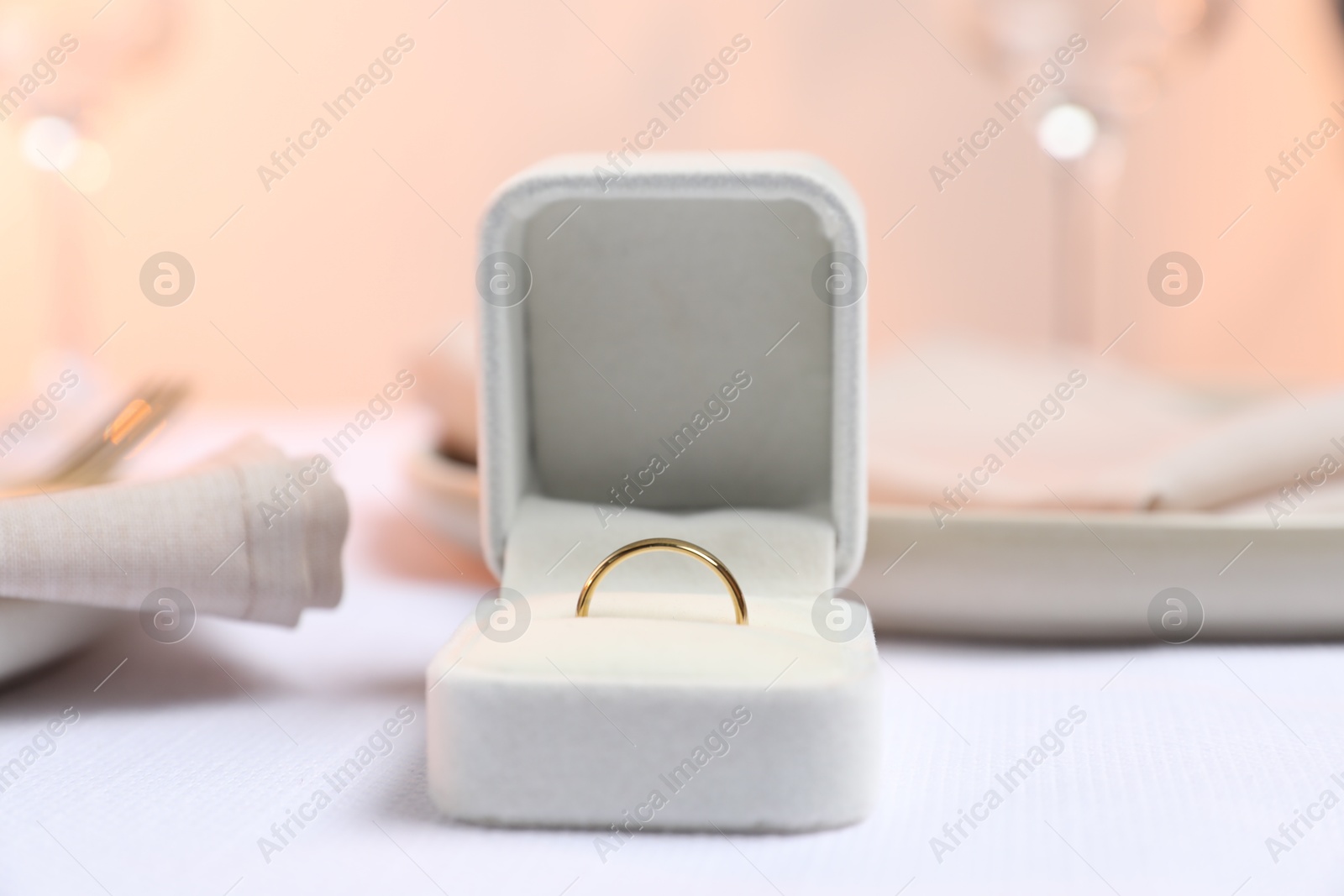 Photo of Beautiful engagement ring and setting for romantic dinner on white table, closeup