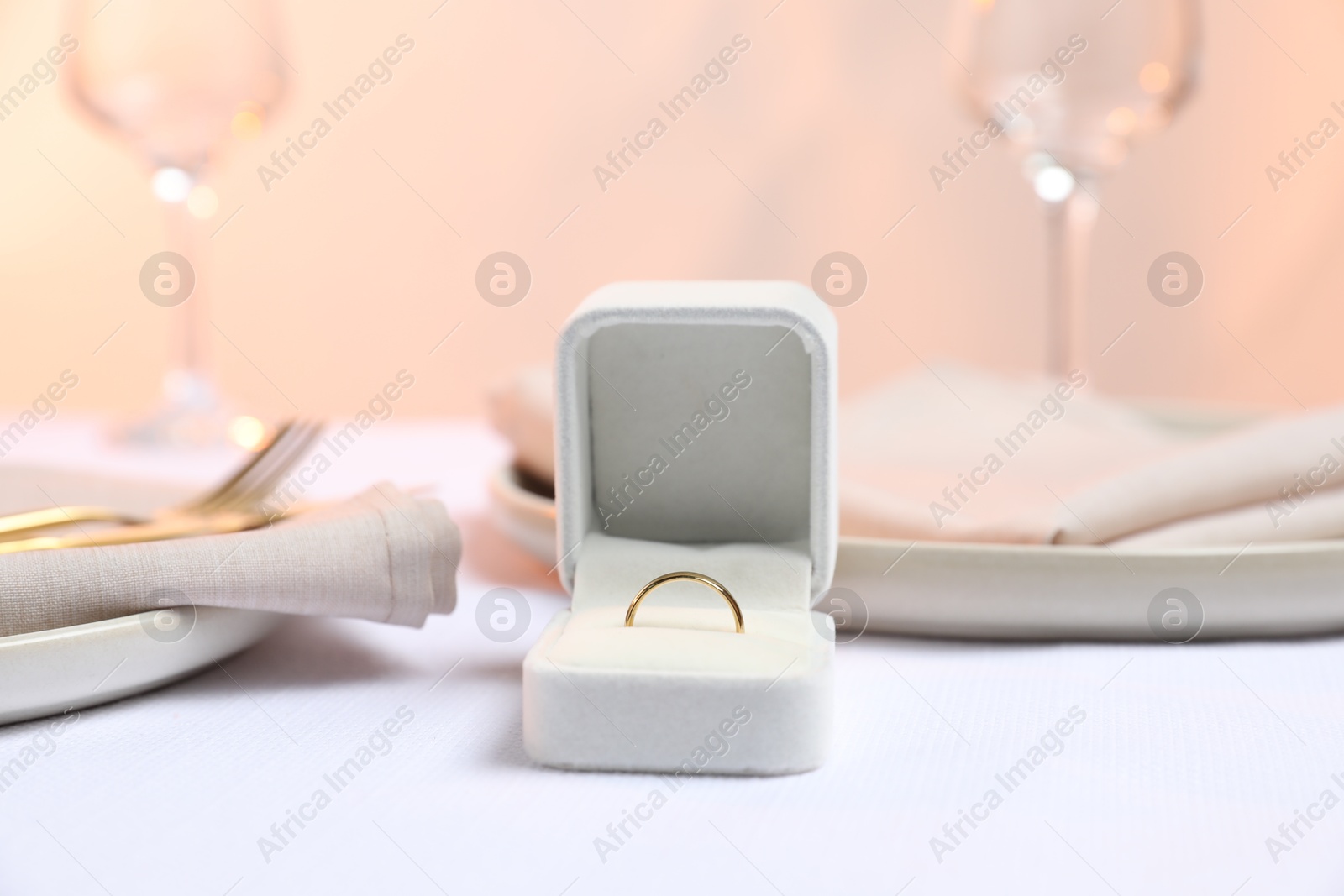 Photo of Beautiful engagement ring and setting for romantic dinner on white table, closeup