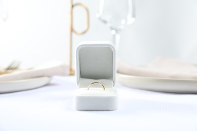 Photo of Beautiful engagement ring and setting for romantic dinner on white table, closeup