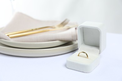 Beautiful engagement ring and setting for romantic dinner on white table, closeup