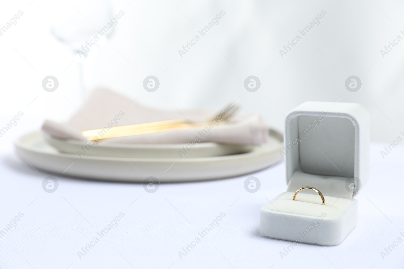 Photo of Beautiful engagement ring and setting for romantic dinner on white table, closeup