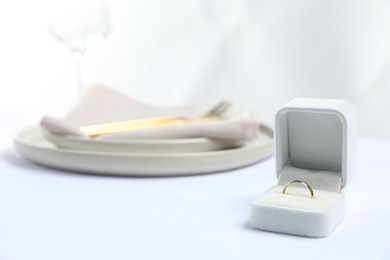 Photo of Beautiful engagement ring and setting for romantic dinner on white table, closeup