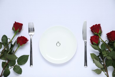 Photo of Engagement ring, rose flowers and tableware on white tablecloth, flat lay. Table setting for romantic dinner