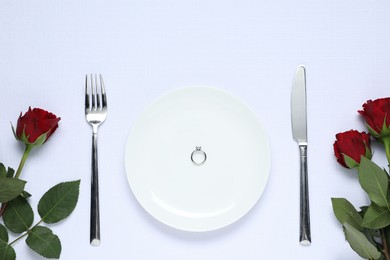 Photo of Engagement ring, rose flowers and tableware on white tablecloth, flat lay. Table setting for romantic dinner