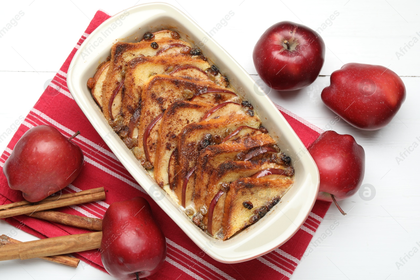 Photo of Delicious bread pudding in baking dish and fresh apples on white wooden table, flat lay