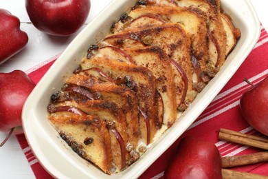 Photo of Delicious bread pudding in baking dish, fresh apples and cinnamon sticks on white table, flat lay