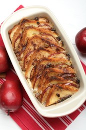 Photo of Delicious bread pudding in baking dish and fresh apples on white table, flat lay