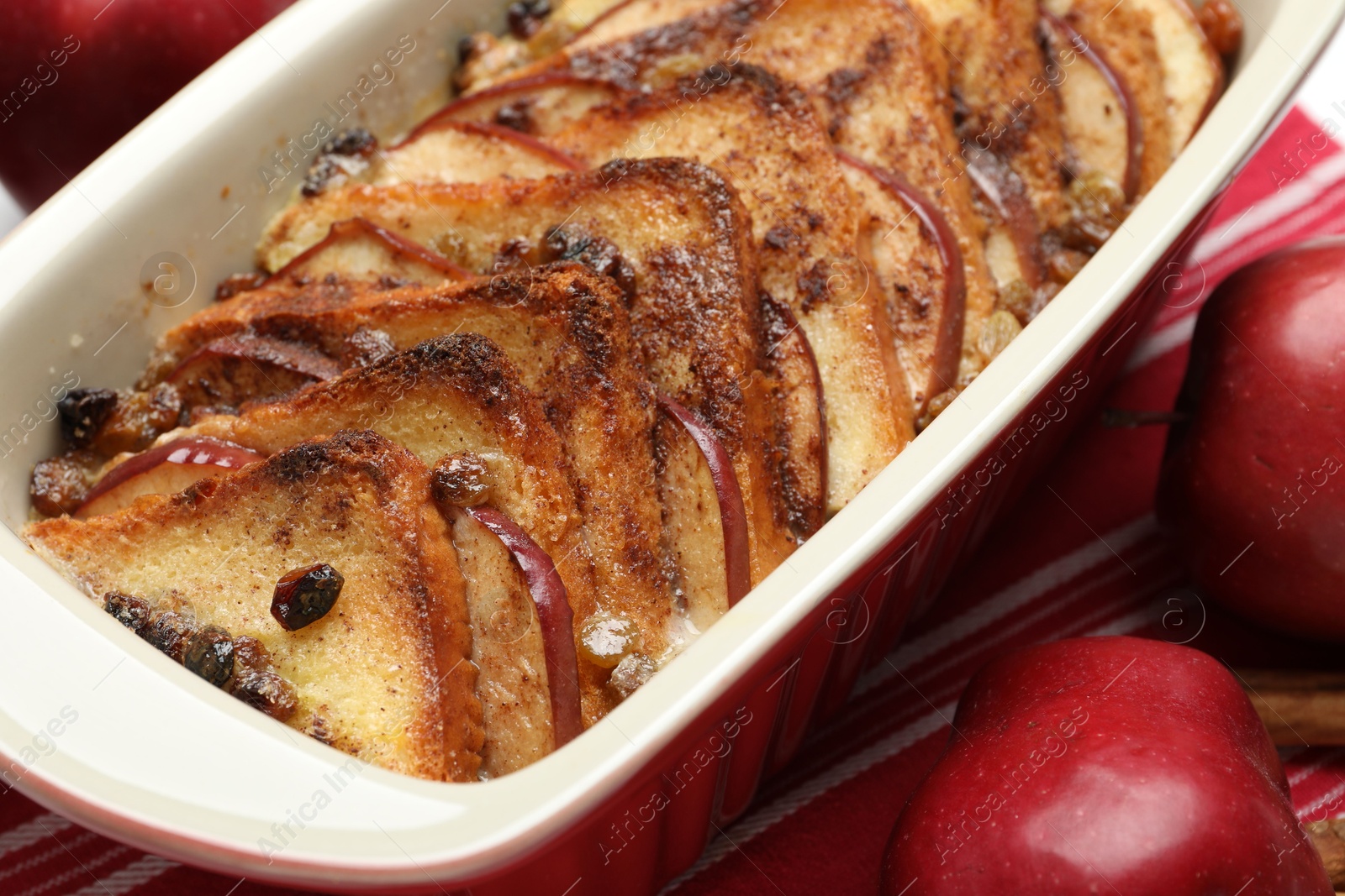 Photo of Delicious bread pudding in baking dish and fresh apples on table, closeup