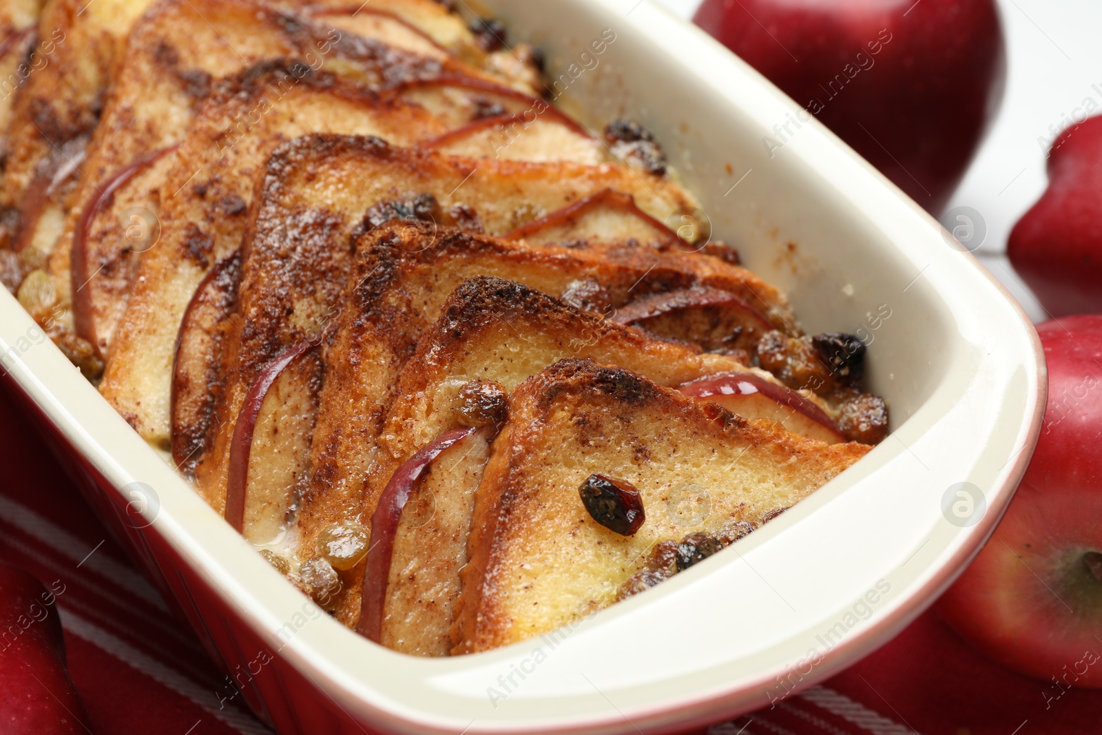 Photo of Delicious bread pudding in baking dish and fresh apples on table, closeup