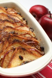 Photo of Delicious bread pudding in baking dish and fresh apples on table, closeup