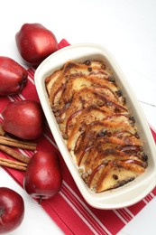 Photo of Delicious bread pudding in baking dish and fresh apples on white wooden table, flat lay