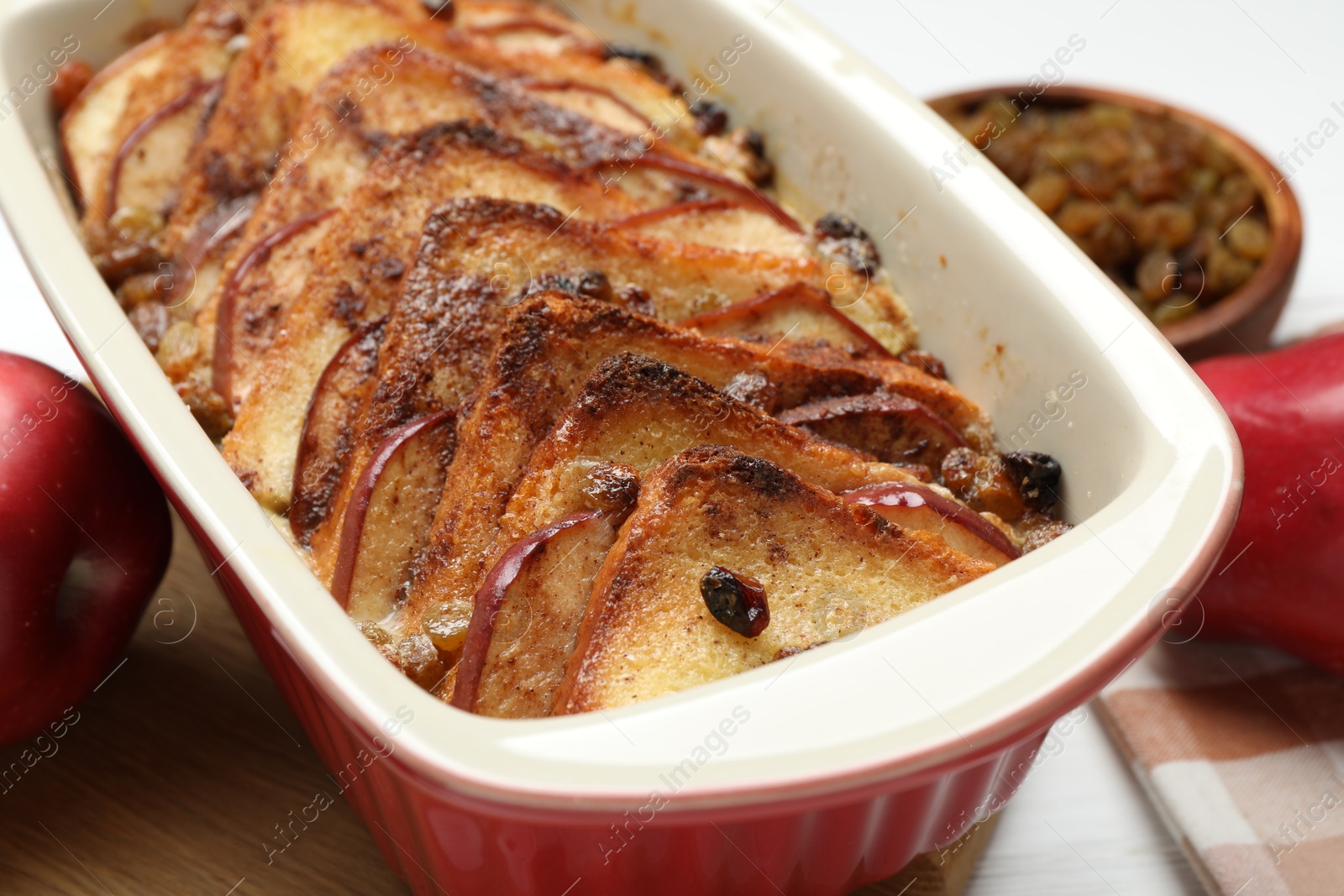 Photo of Delicious bread pudding in baking dish and fresh apples on table, closeup