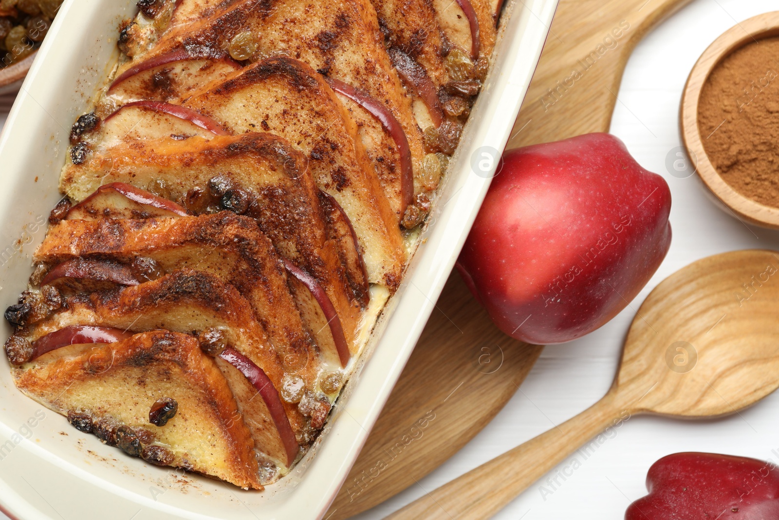 Photo of Delicious bread pudding in baking dish, fresh apples and cinnamon on white table, flat lay