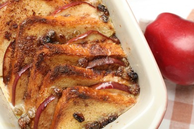 Photo of Delicious bread pudding in baking dish and fresh apple on table, closeup