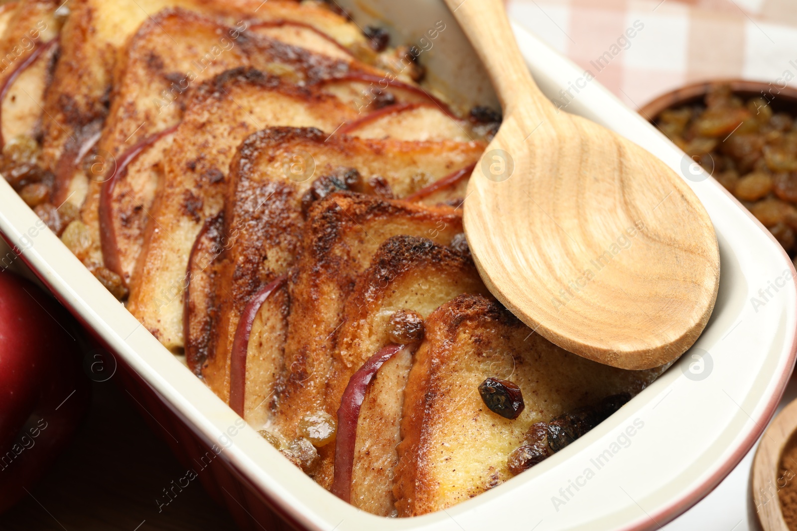 Photo of Delicious bread pudding in baking dish and spoon on table, closeup