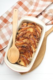 Photo of Delicious bread pudding in baking dish and spoon on white wooden table, top view