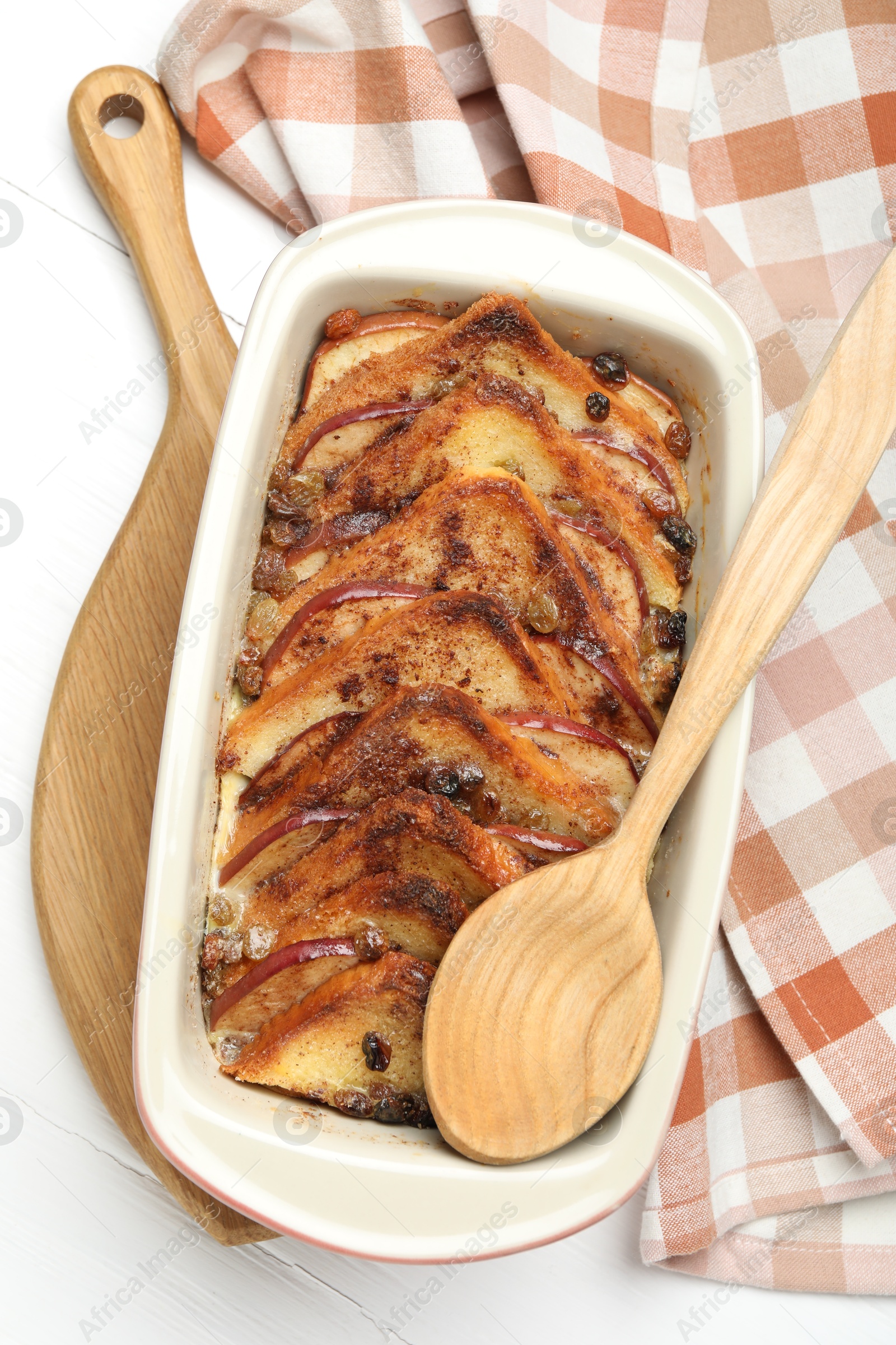 Photo of Delicious bread pudding in baking dish and spoon on white wooden table, top view