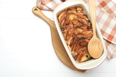 Photo of Delicious bread pudding in baking dish and spoon on white wooden table, top view. Space for text