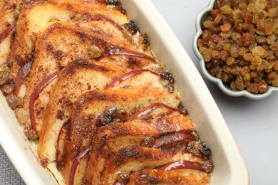 Photo of Delicious bread pudding in baking dish and raisins on light gray table, flat lay