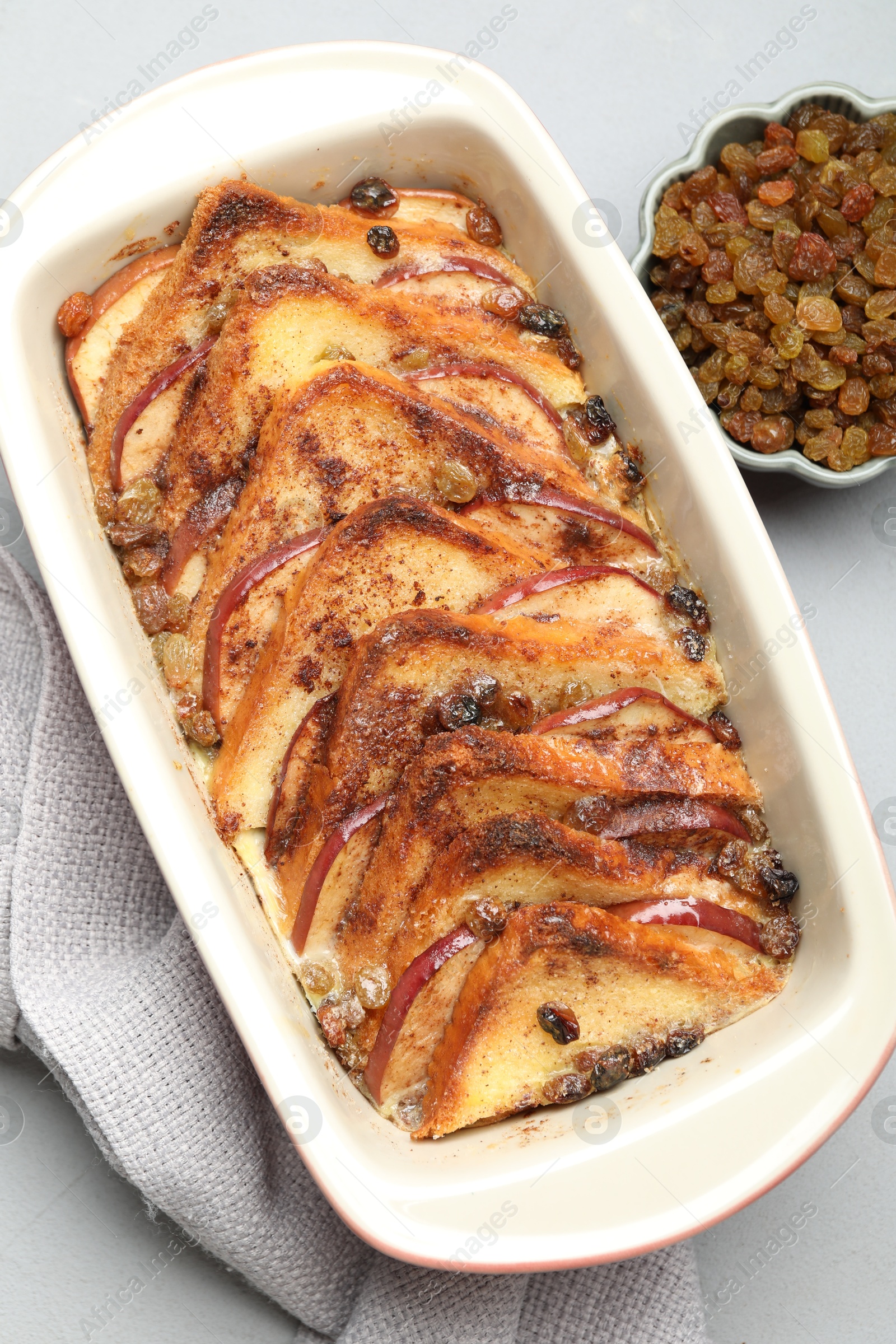 Photo of Delicious bread pudding in baking dish and raisins on light gray table, flat lay