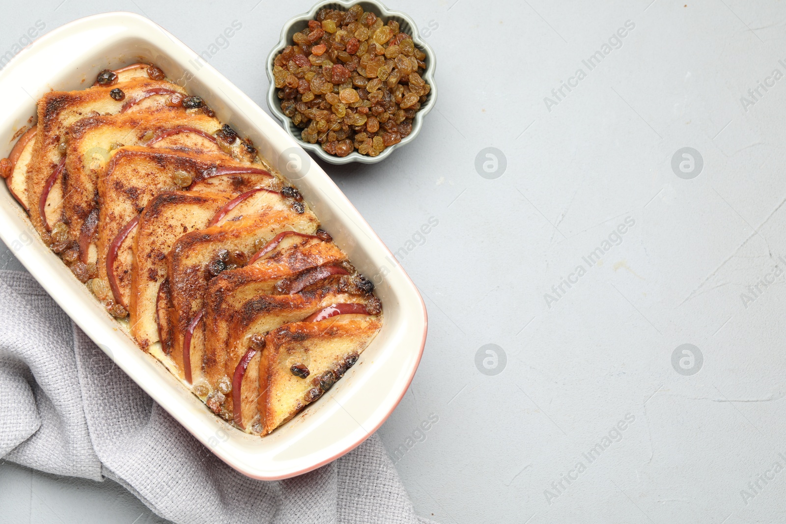 Photo of Delicious bread pudding in baking dish and raisins on light gray table, flat lay. Space for text