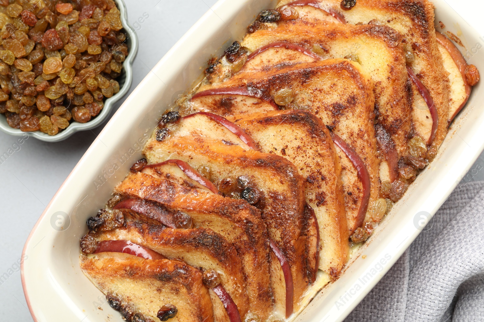 Photo of Delicious bread pudding in baking dish and raisins on light gray table, flat lay