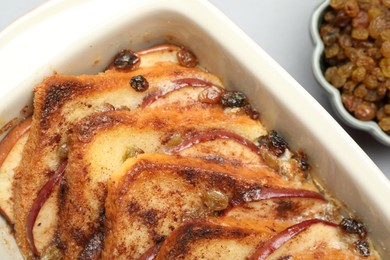 Photo of Delicious bread pudding in baking dish and raisins on light gray table, closeup