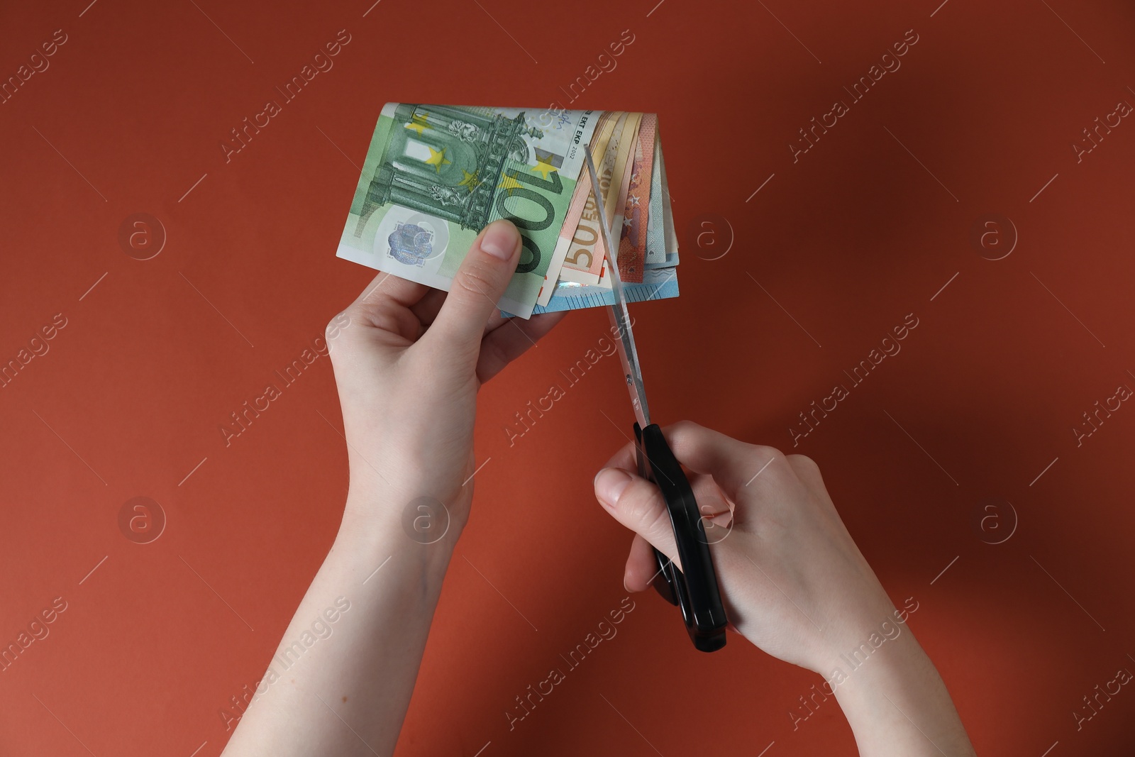 Photo of Woman cutting euro banknotes on brown background, top view