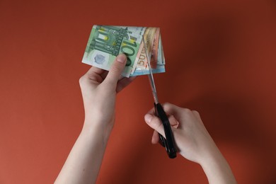 Photo of Woman cutting euro banknotes on brown background, top view