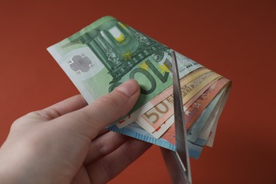 Photo of Woman cutting euro banknotes on brown background, closeup