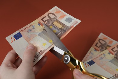 Woman cutting euro banknotes on brown background, closeup