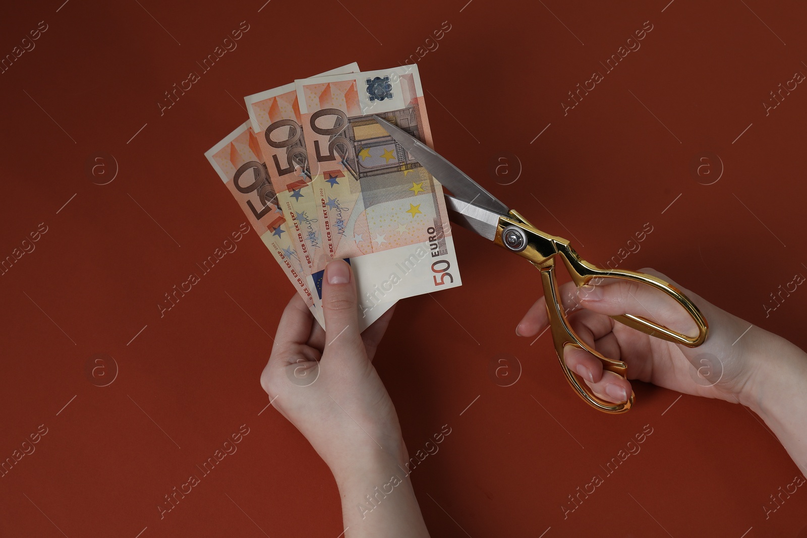 Photo of Woman cutting euro banknotes on brown background, top view