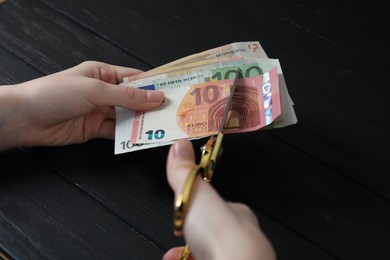 Photo of Woman cutting euro banknotes at black wooden table, closeup