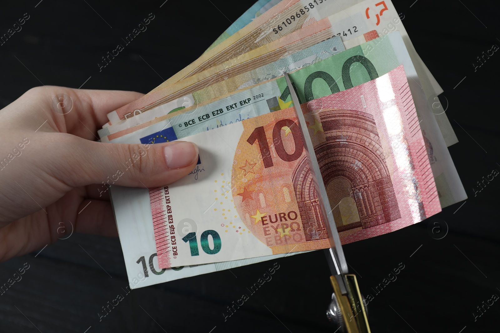 Photo of Woman cutting euro banknotes at black table, closeup