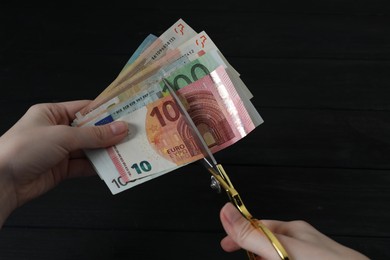 Photo of Woman cutting euro banknotes at black wooden table, closeup