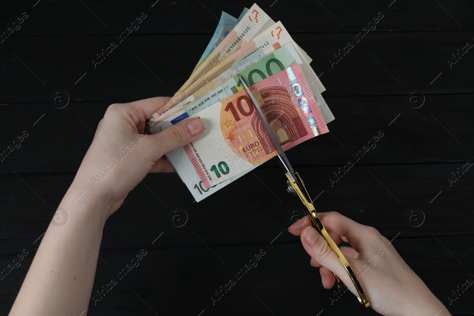 Photo of Woman cutting euro banknotes at black wooden table, top view