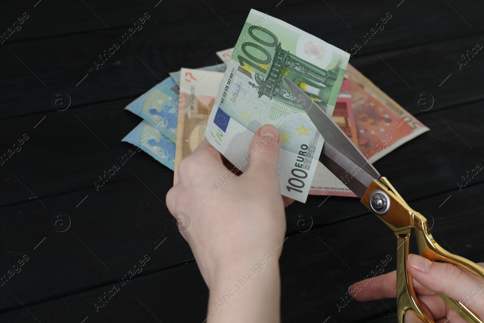 Photo of Woman cutting euro banknotes at black wooden table, closeup