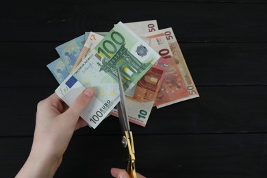 Photo of Woman cutting euro banknotes at black wooden table, closeup