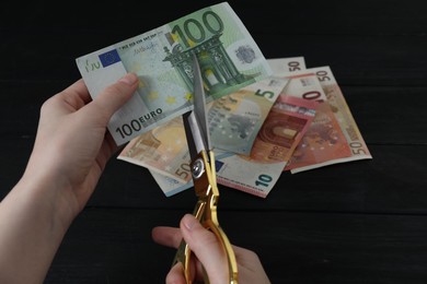 Photo of Woman cutting euro banknotes at black wooden table, closeup